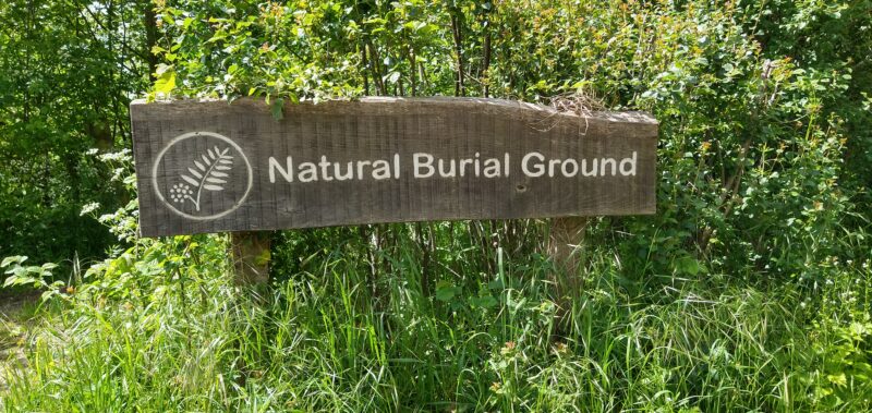 Wooden sign surrounded by green leaves saying, 'Natural Burial Ground'.